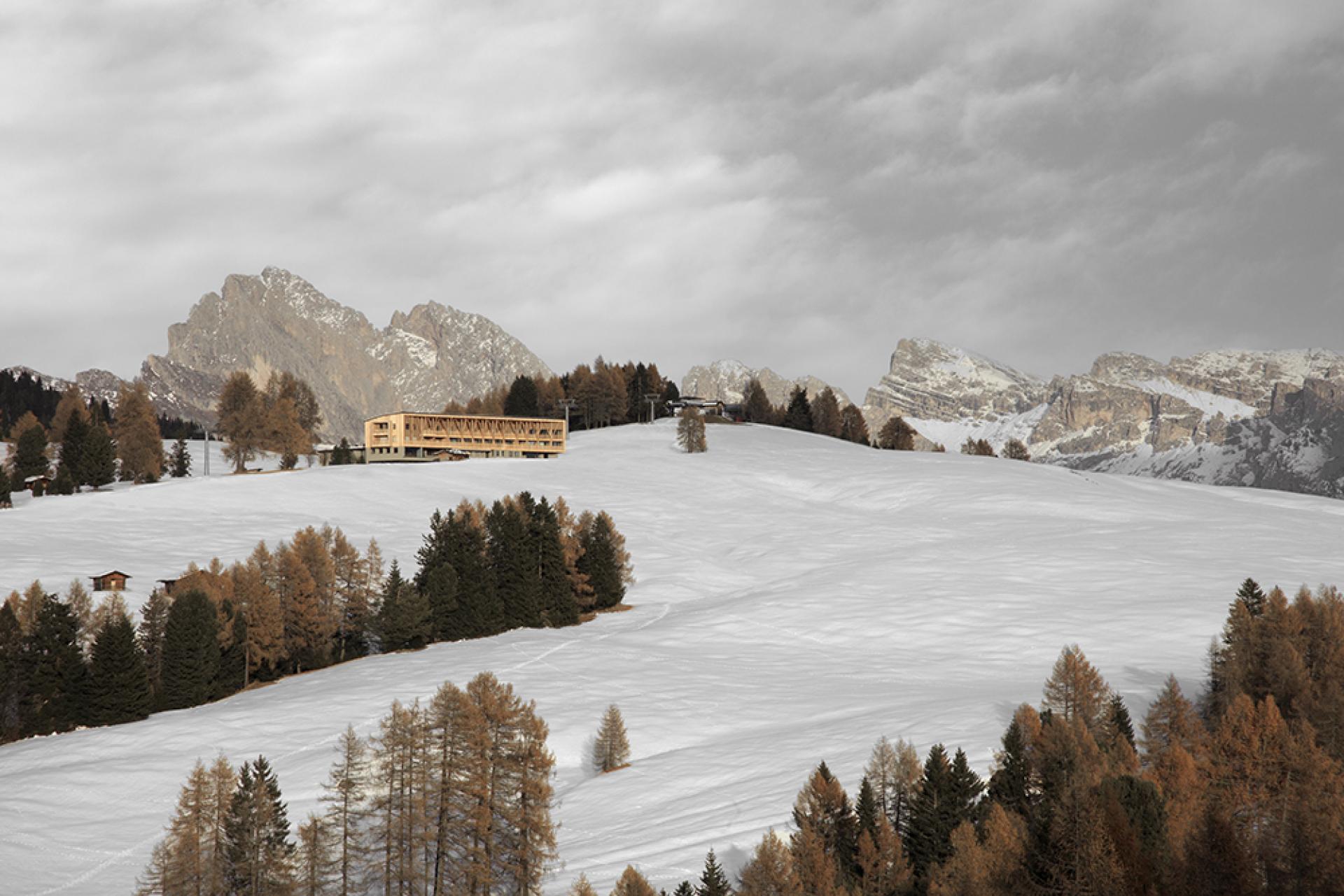 Icaro Hotel set against the Dolomite Mountains, surrounded by snow-covered slopes and autumnal trees, showcasing alpine architecture.