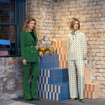 Tekla Severin and Ramona Macchi pose beside colorful tiles and floral arrangements, highlighting the Färgblock collection's playful design.