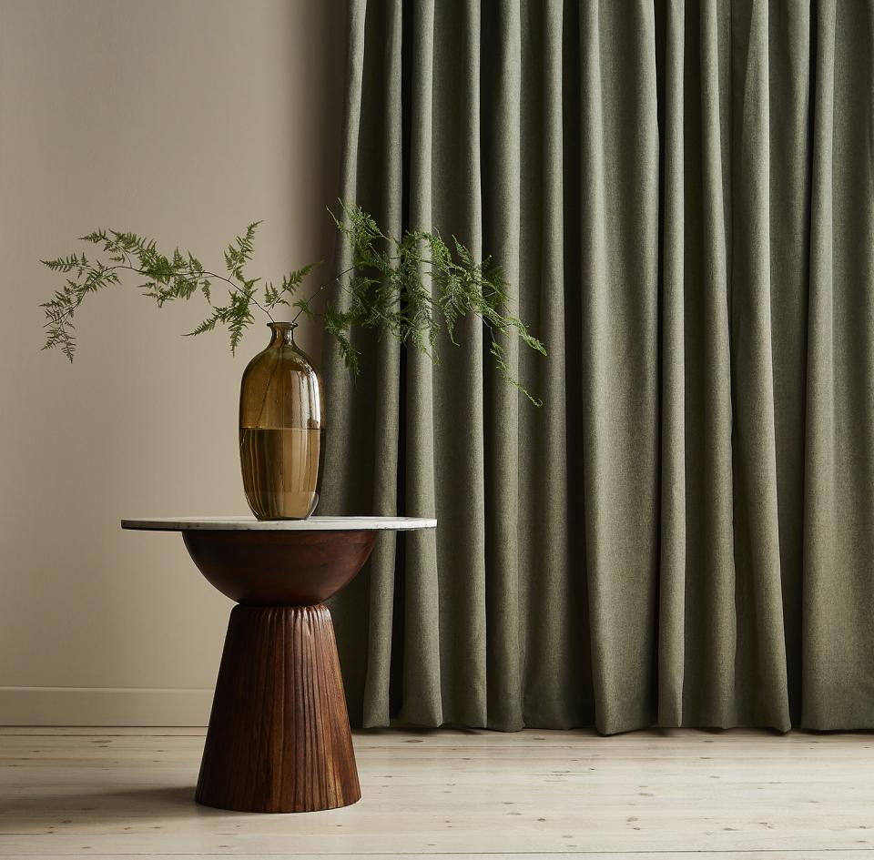 Green curtains from the Tundra collection by ILIV complement a stylish wooden table and a decorative vase.