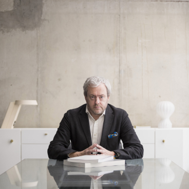 Mark Simpson, principal and head of design at BDP, seated at a modern glass table in an industrial workspace.