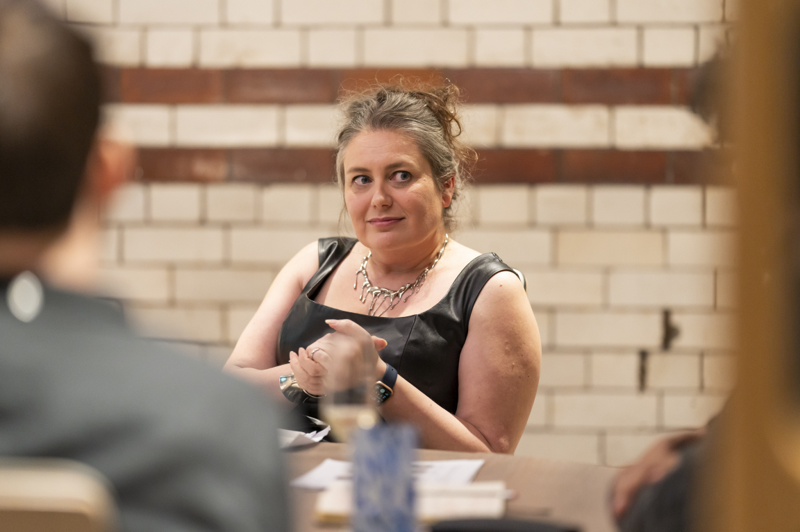 A woman in a black dress engages in a discussion about technology and sustainability in design at a roundtable meeting.