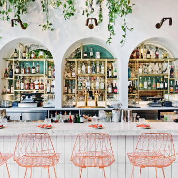 Contemporary bar with Moroccan design elements, featuring vibrant orange chairs and a well-stocked liquor display.