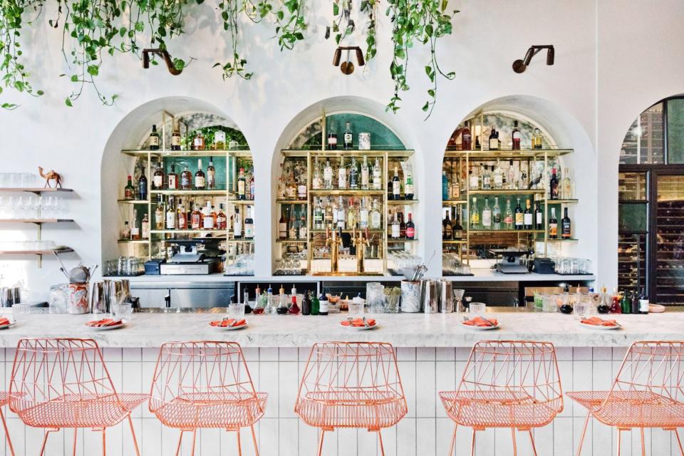Contemporary bar with Moroccan design elements, featuring vibrant orange chairs and a well-stocked liquor display.