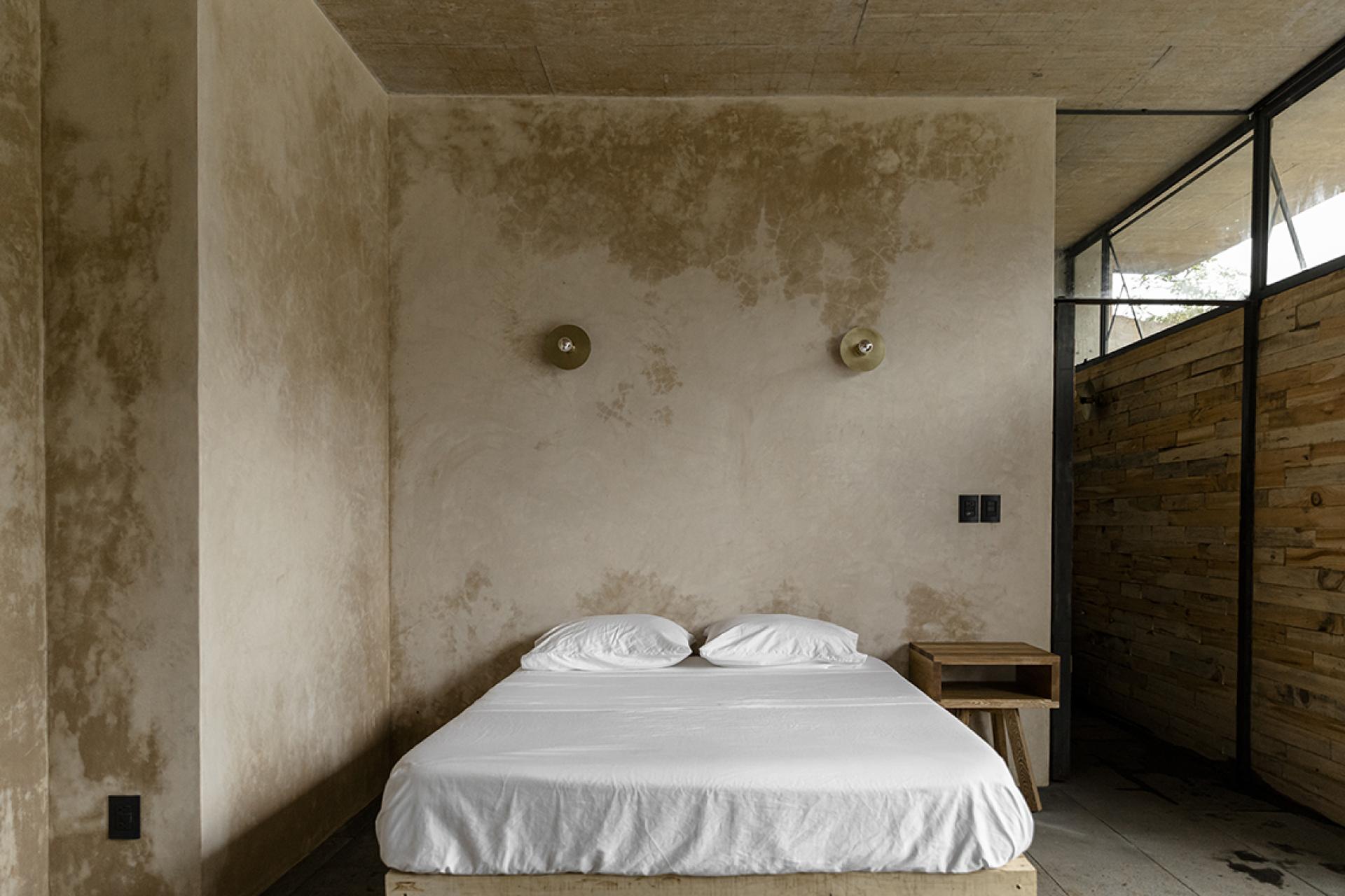 Minimalist bedroom interior of Avocado House, featuring a wooden bed, soft linens, and natural textured walls.