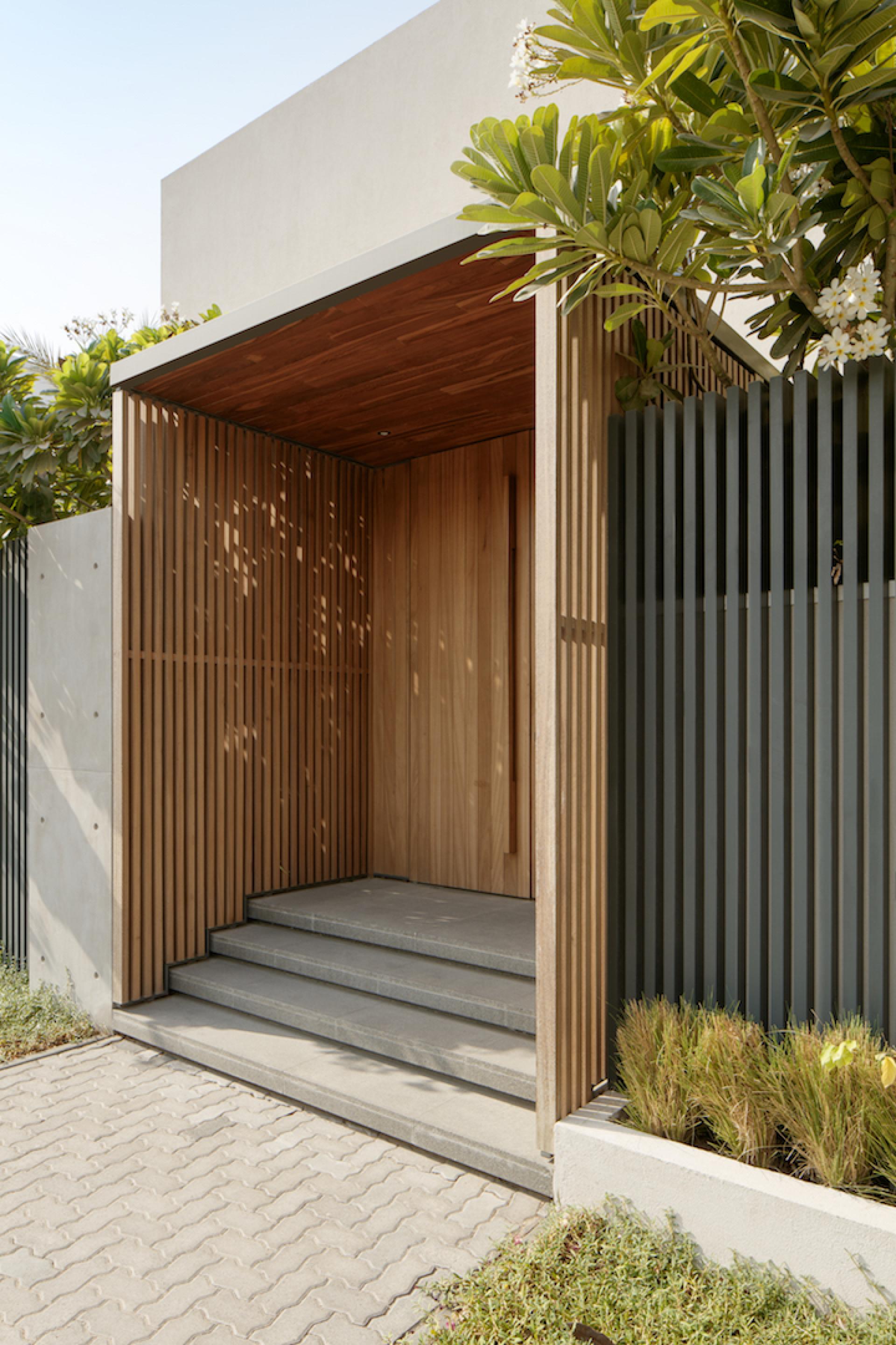 Elegant entrance to Villa Jumeirah, featuring wooden slats and a serene walkway surrounded by lush greenery.