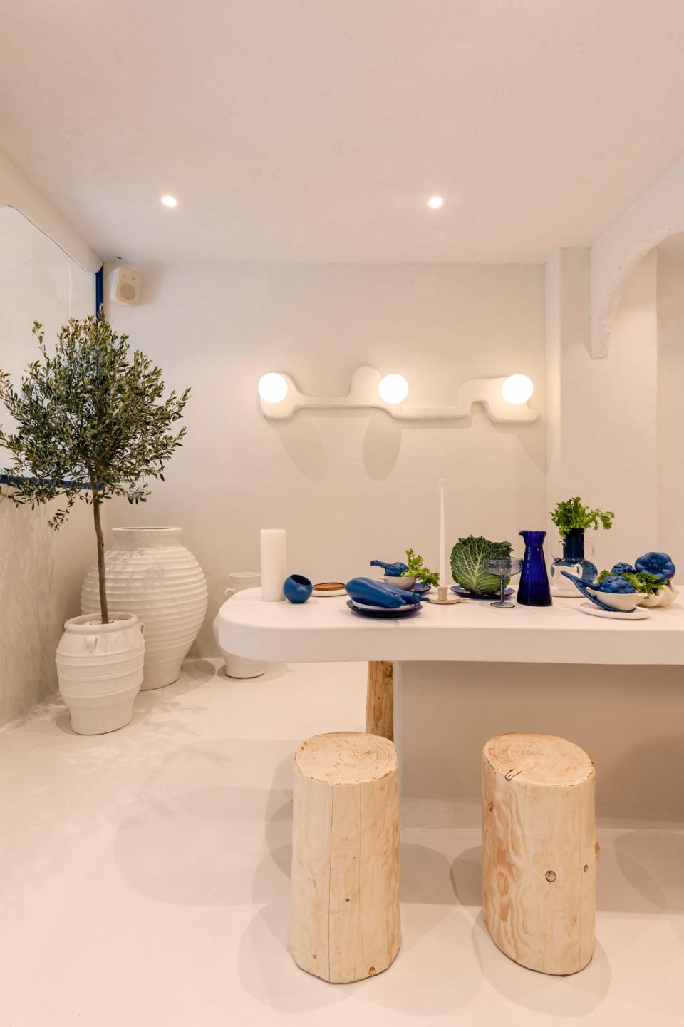Modern Greek restaurant interior featuring a sleek white table, natural wood stools, and vibrant blue dishware.