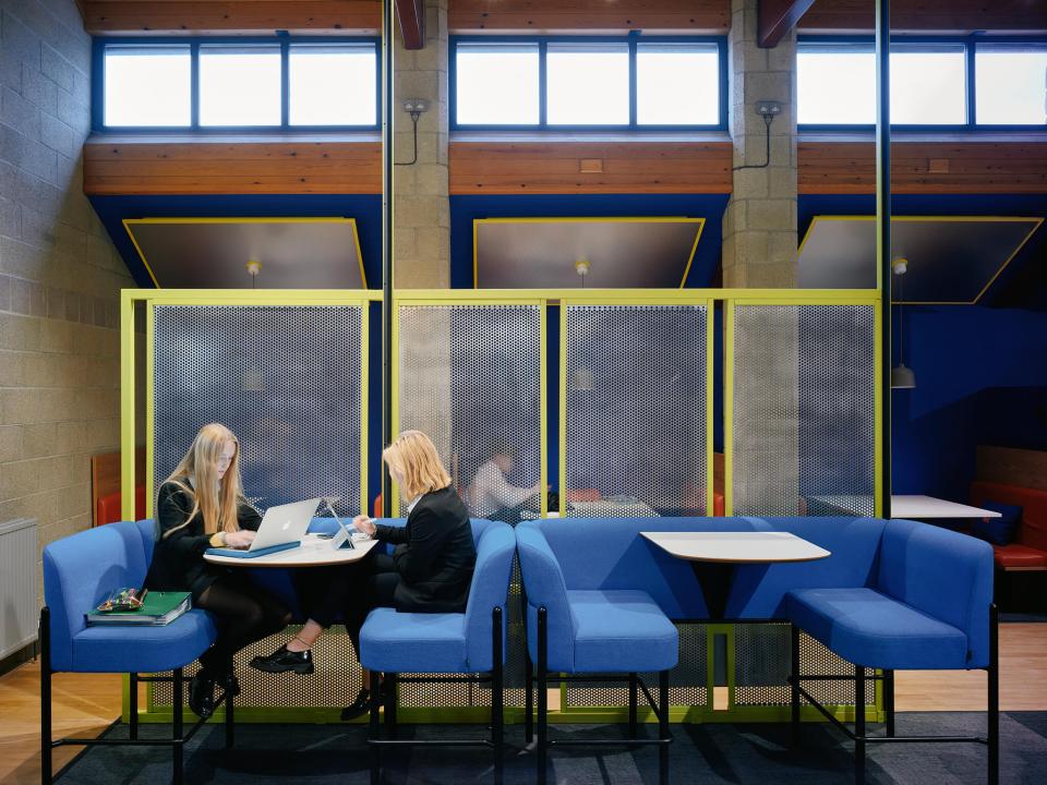 Brightly lit study area at Sedbergh School's Queens Hall, featuring modern seating and students engaging with laptops.