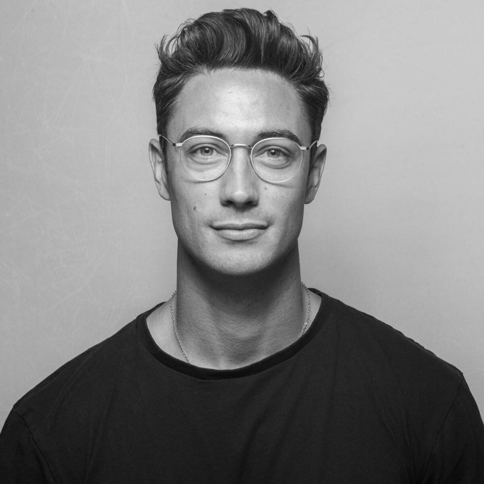 Jamie Hanson, director at CODA Studios, poses confidently in a black shirt and glasses against a light backdrop.