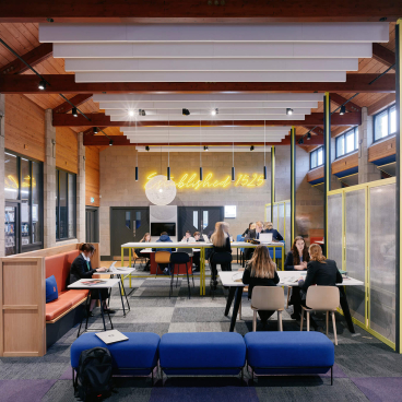 Modern interior of Sedbergh School's Queens Hall featuring students studying, colorful furniture, and striking lighting elements.