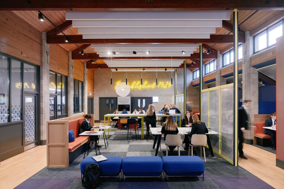 Modern interior of Sedbergh School's Queens Hall featuring students studying, colorful furniture, and striking lighting elements.