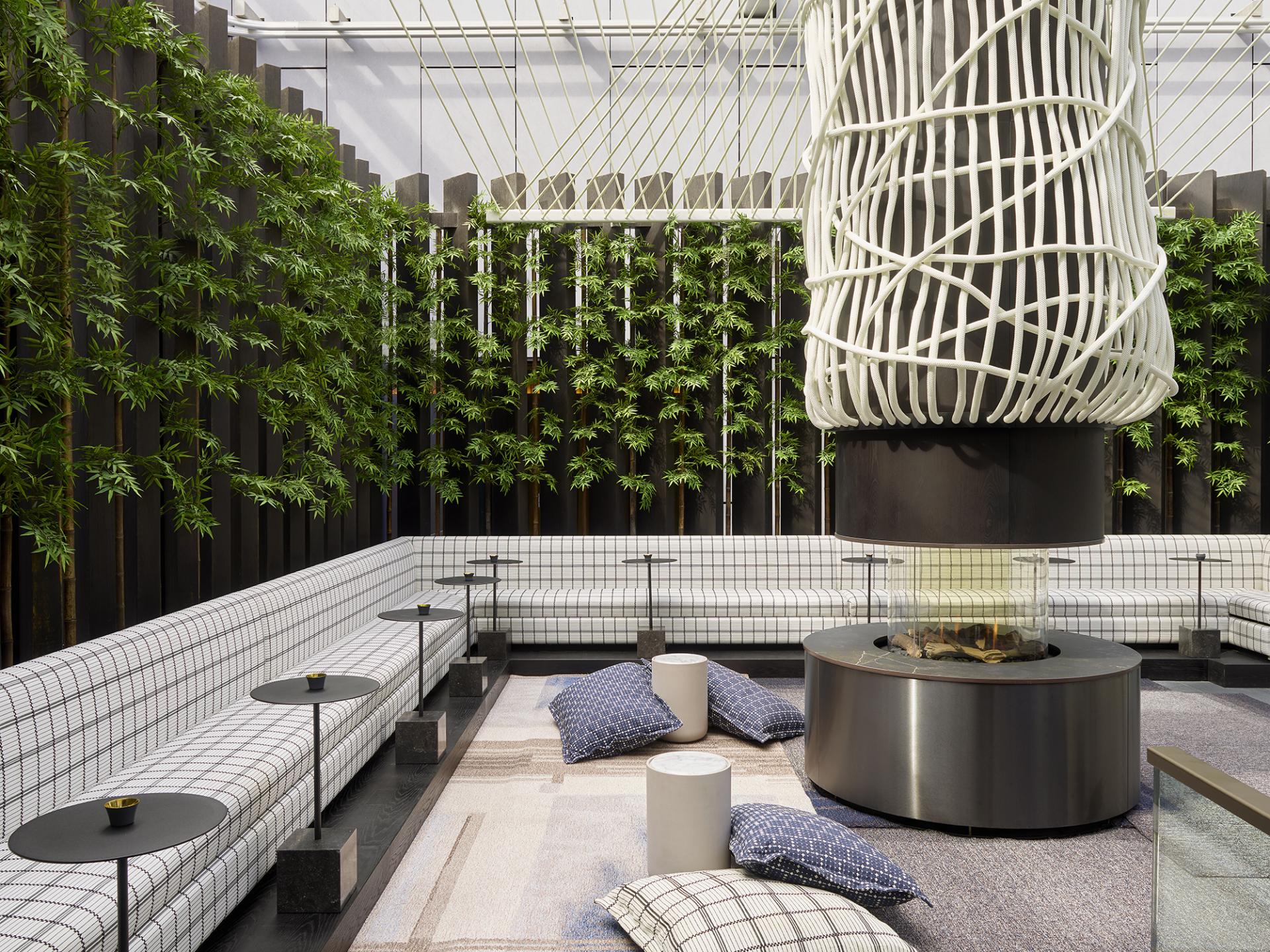 Stylish hotel lounge featuring green plants, plush seating, and a central modern fireplace, designed by Yabu Pushelberg.