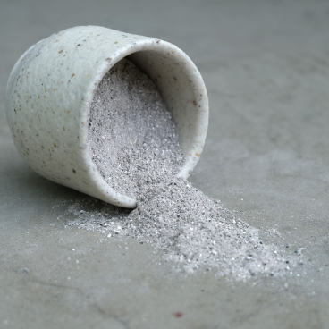 Ceramic container spilling innovative grey material, showcasing trends in surface design and material innovation at the Surface Design Show.