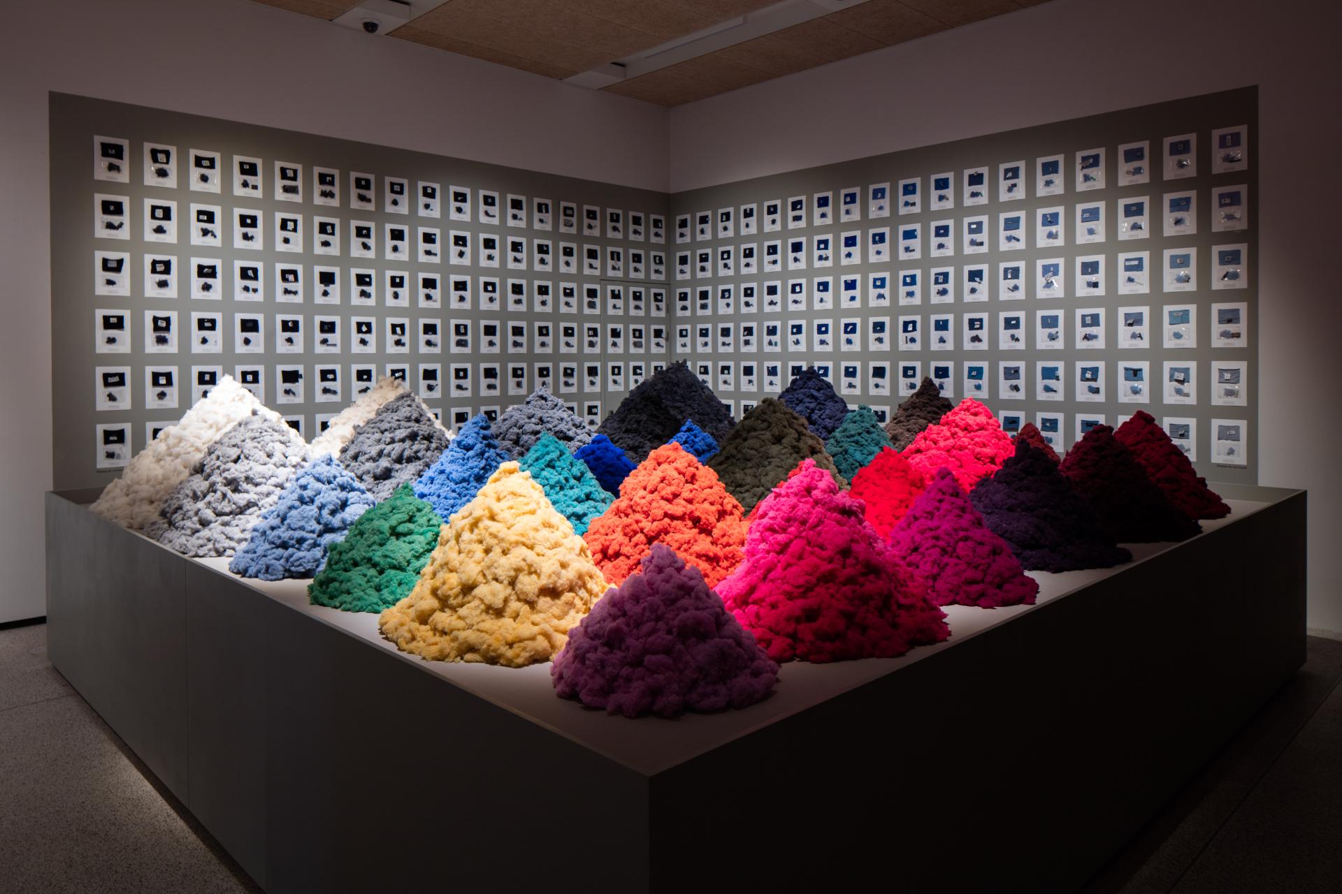 Colorful textile material mounds displayed in a contemporary museum setting, illustrating Christien Meindertsma's innovative design approach with materials.