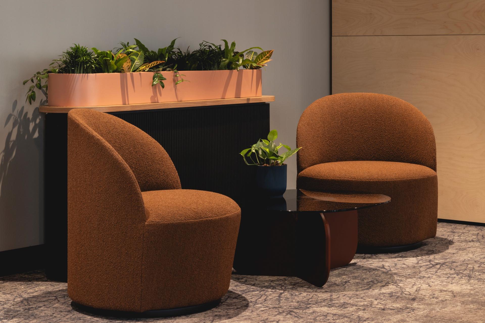 Art Deco-inspired seating area featuring curved chairs, a sleek table, and lush plants for a calming workplace ambience.