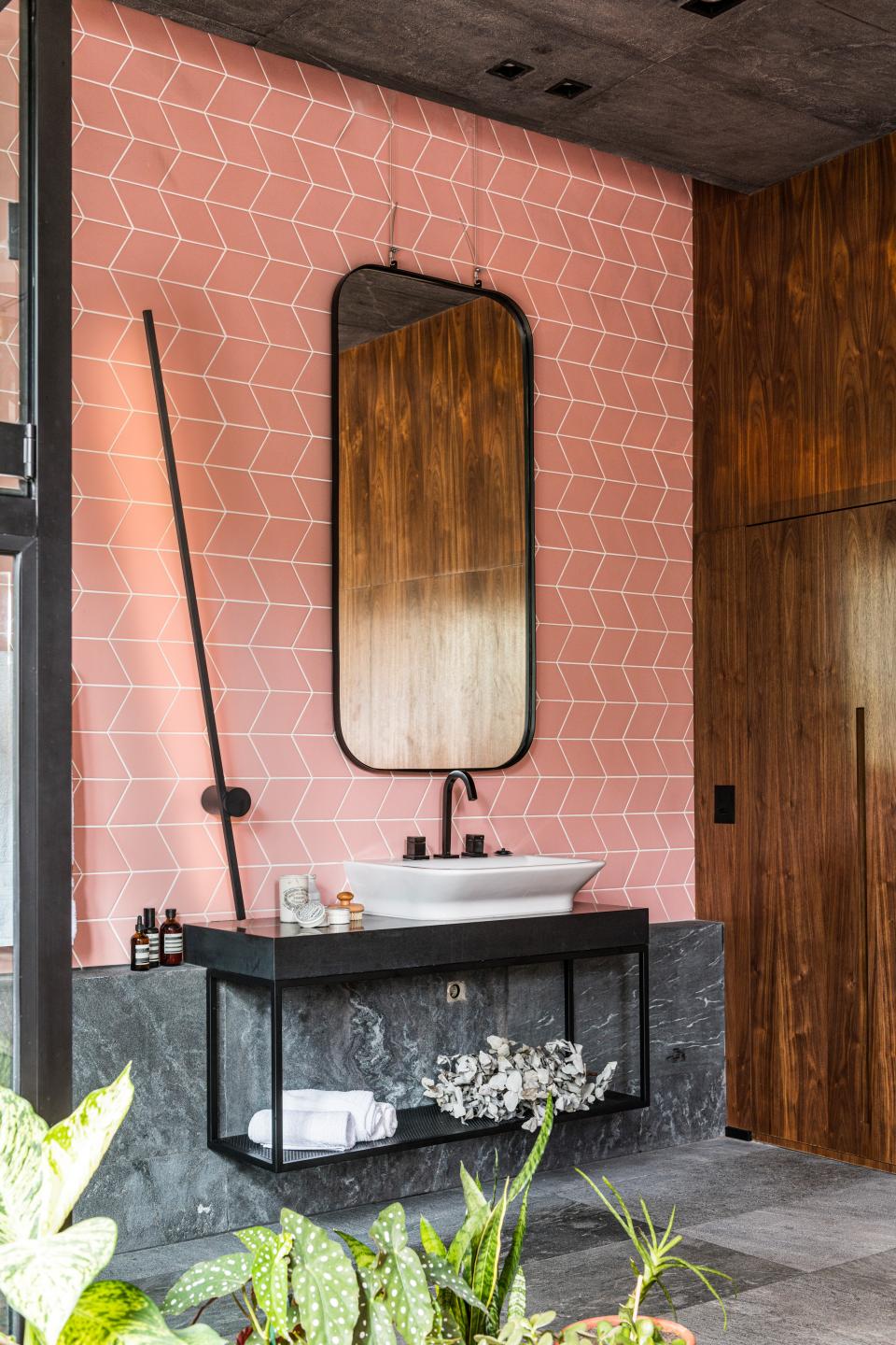 Modern bathroom design featuring a pink geometric tile wall, black fixtures, and natural greenery for a harmonious atmosphere.