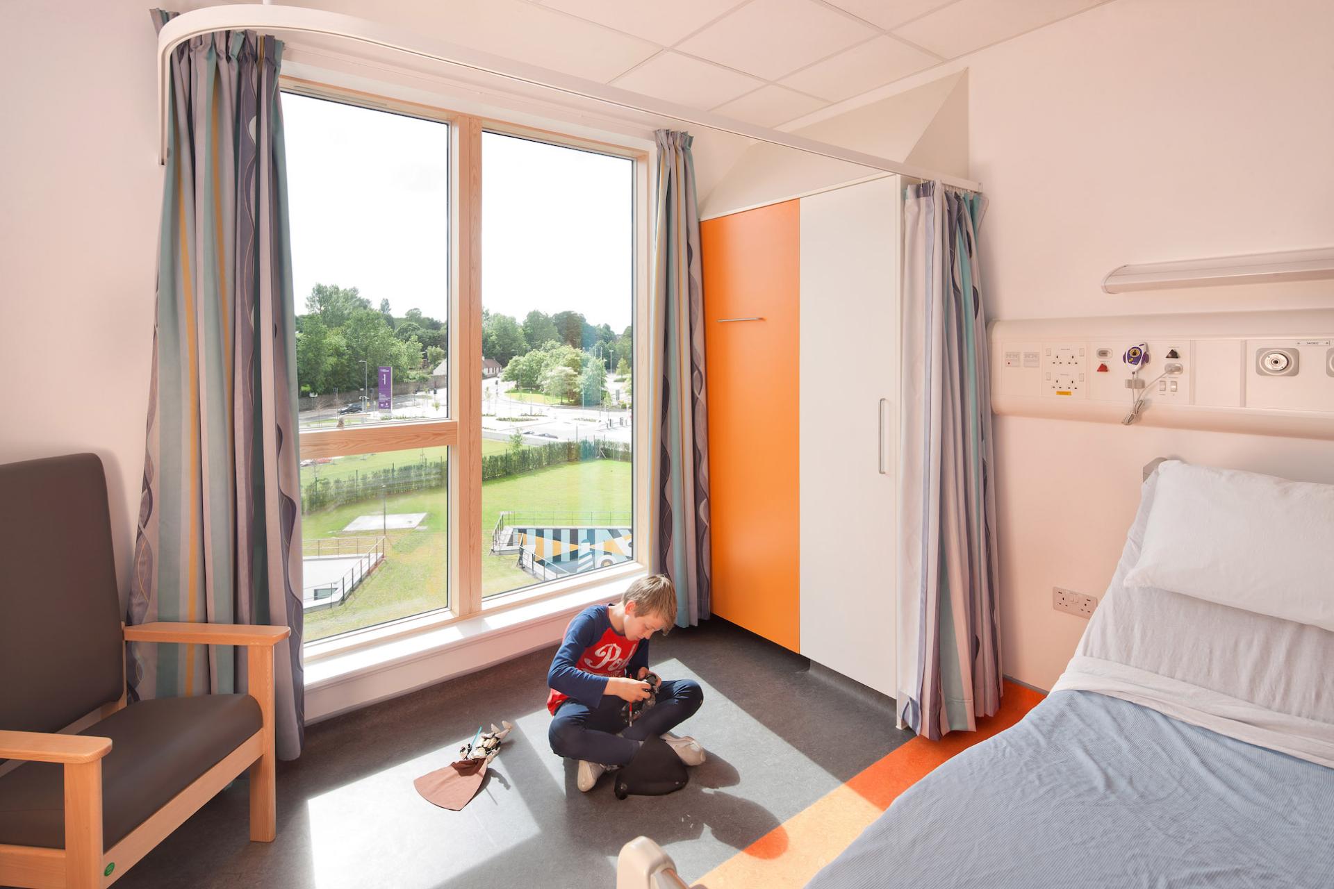 Bright, welcoming patient room featuring a child playing on the floor, large windows, and modern healthcare design elements.