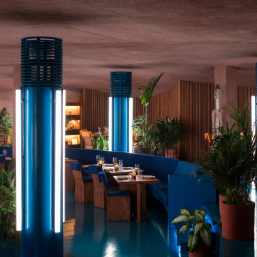 Futuristic dining space in Desa Potato Head, featuring vibrant blue lighting, earthy decor, and lush greenery.