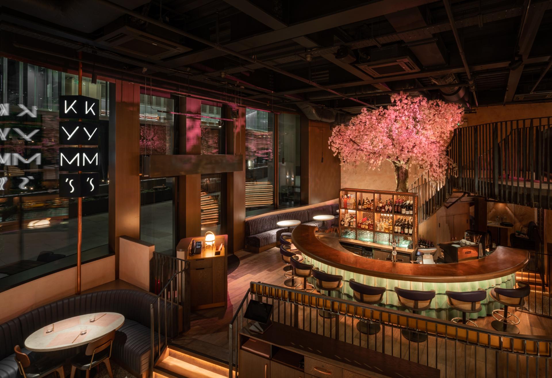 Stylish interior of Chef Andrew Wong's restaurant featuring a cherry blossom tree and a curved bar at Bloomberg Arcade.