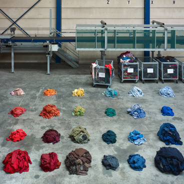 Colorfully arranged fabric piles on a warehouse floor, showcasing Christien Meindertsma's exploration of material reuse at Vitra Design Museum.