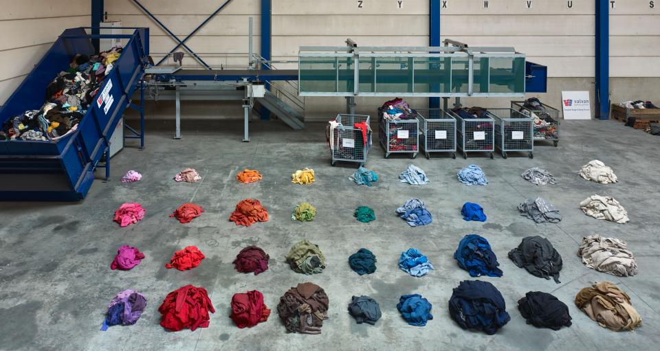 Colorfully arranged fabric piles on a warehouse floor, showcasing Christien Meindertsma's exploration of material reuse at Vitra Design Museum.