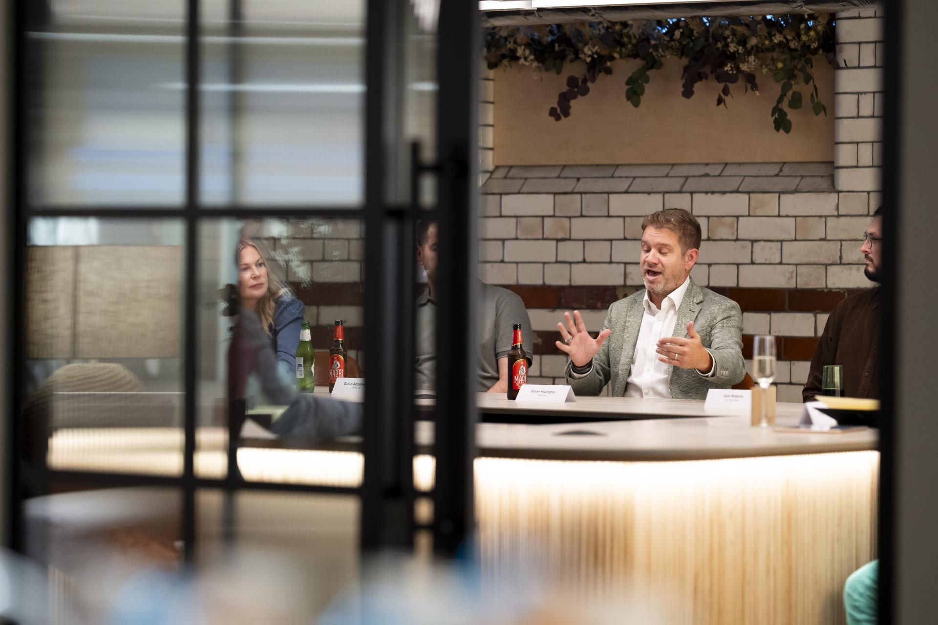 Roundtable discussion with participants engaging in conversation about data's impact on the workplace, surrounded by beverages and a modern interior.