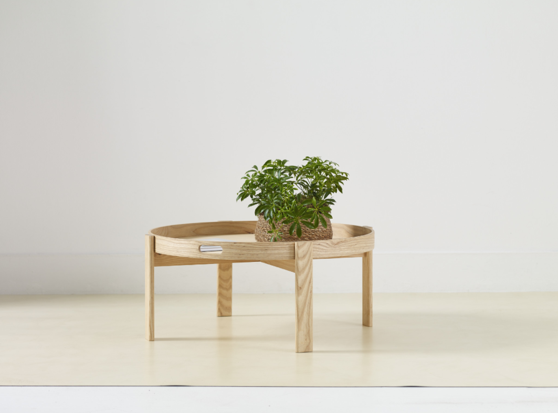 Round wooden table with legs, featuring a potted plant, showcasing sustainable furniture design for wellbeing.