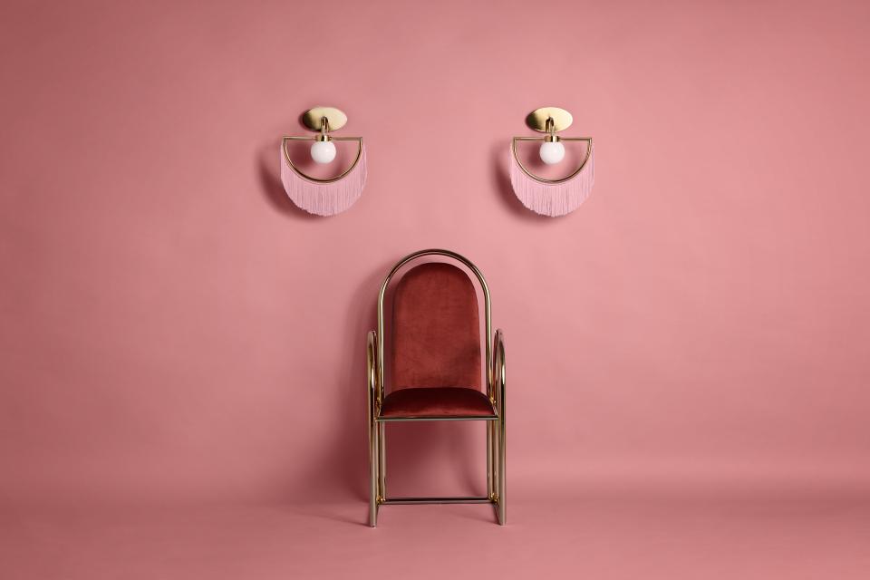 Vintage-inspired chair with elegant gold accents, set against a soft pink background, complemented by stylish wall lamps.