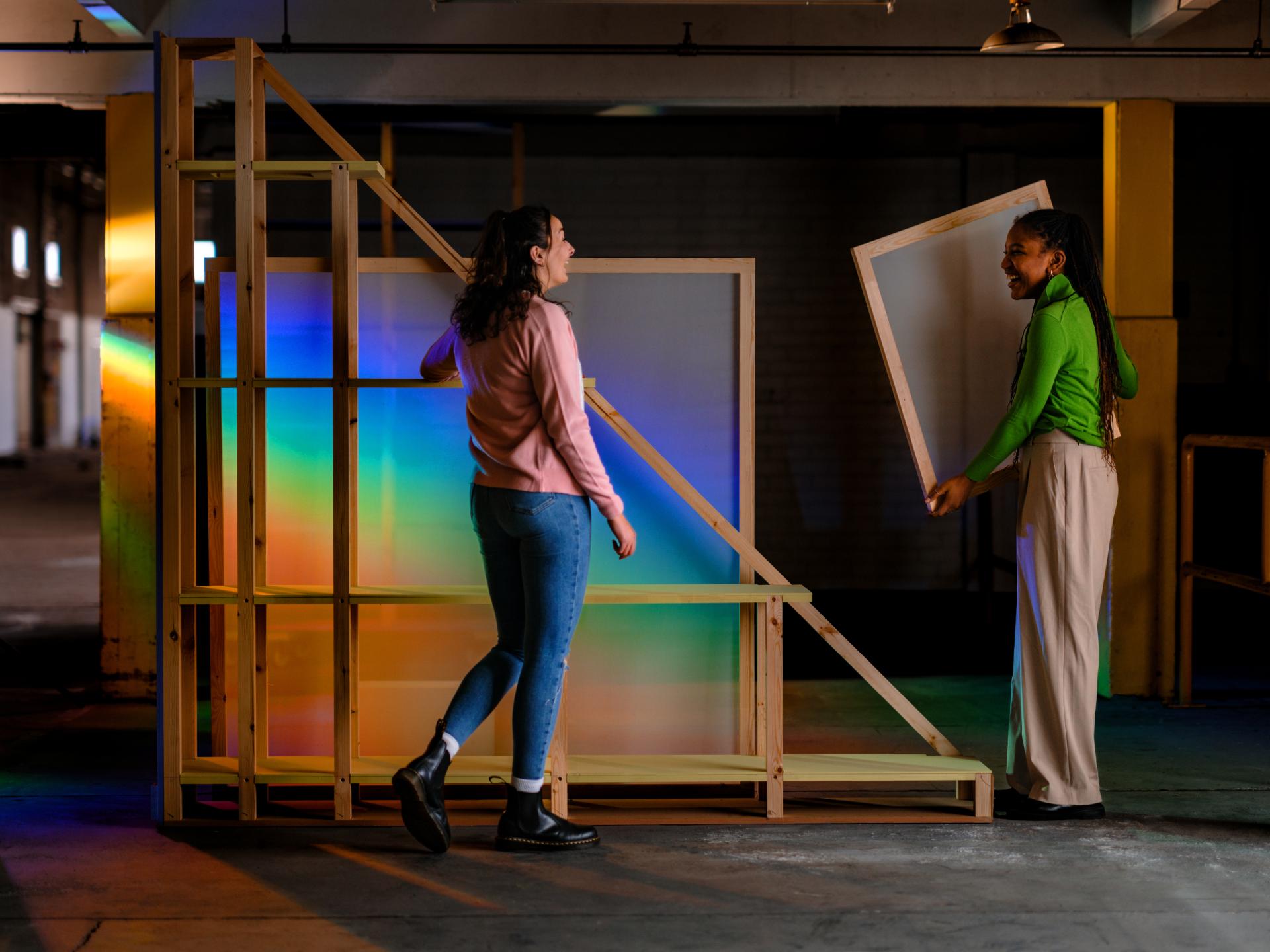 Two women collaboratively assembling a colorful, transparent exhibition design structure for Dundee Design Festival 2024.