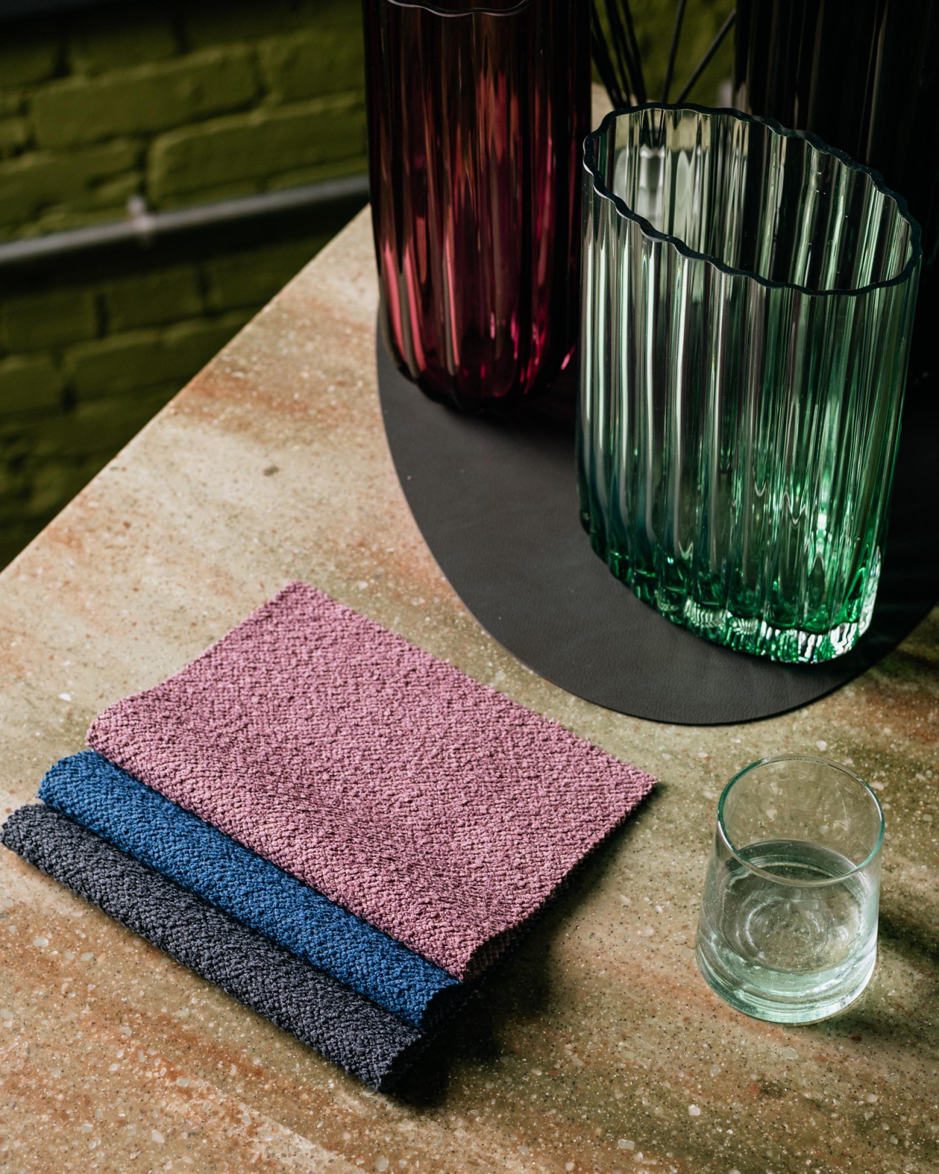 Eden and Bouclé performance upholstery fabrics in soft textures, displayed with colorful glass vases on a stylish surface.