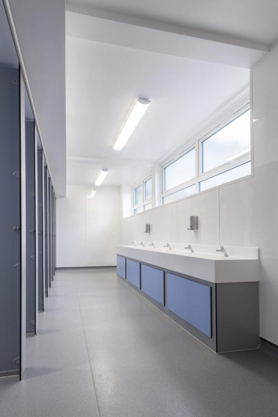 Modern boys' washroom at Stretford Grammar featuring sleek cubicle systems, spacious sinks, and ample natural light.