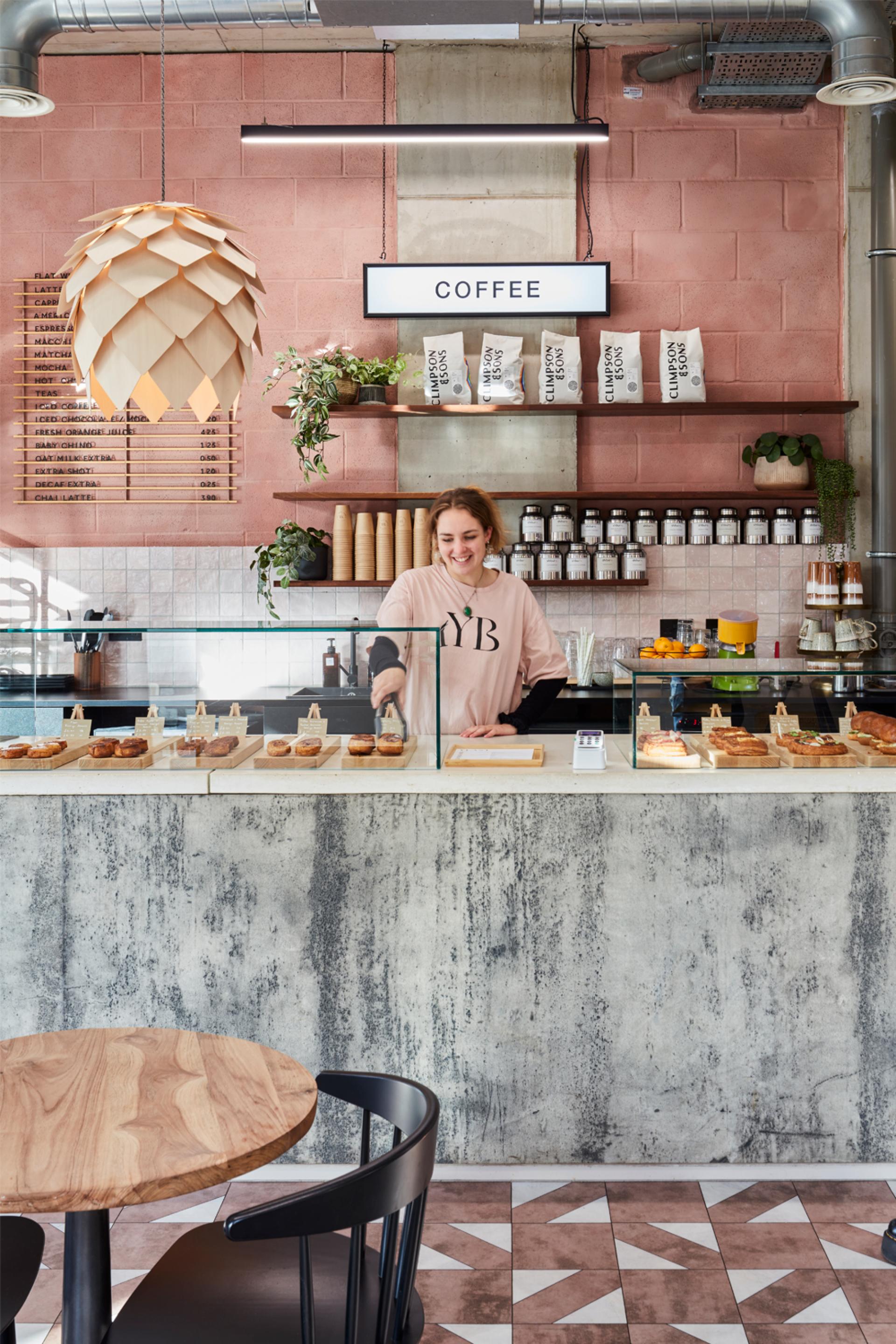 A barista in a stylish bakery serves pastries at a modern counter adorned with urban design elements.