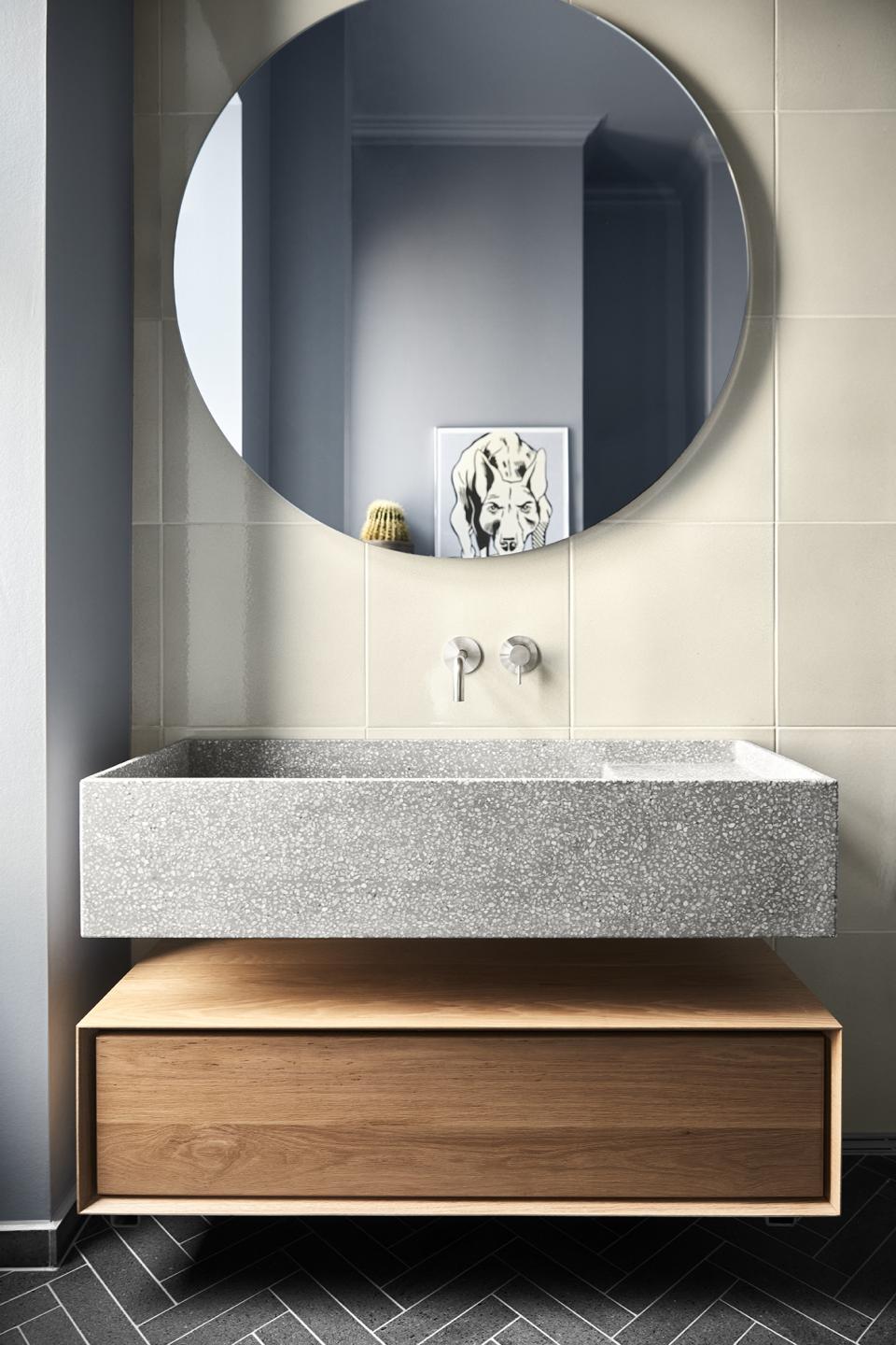 Modern bathroom featuring a gray stone sink, circular mirror, and wooden drawer, designed by Emil Thorup using d line's Qtoo collection.