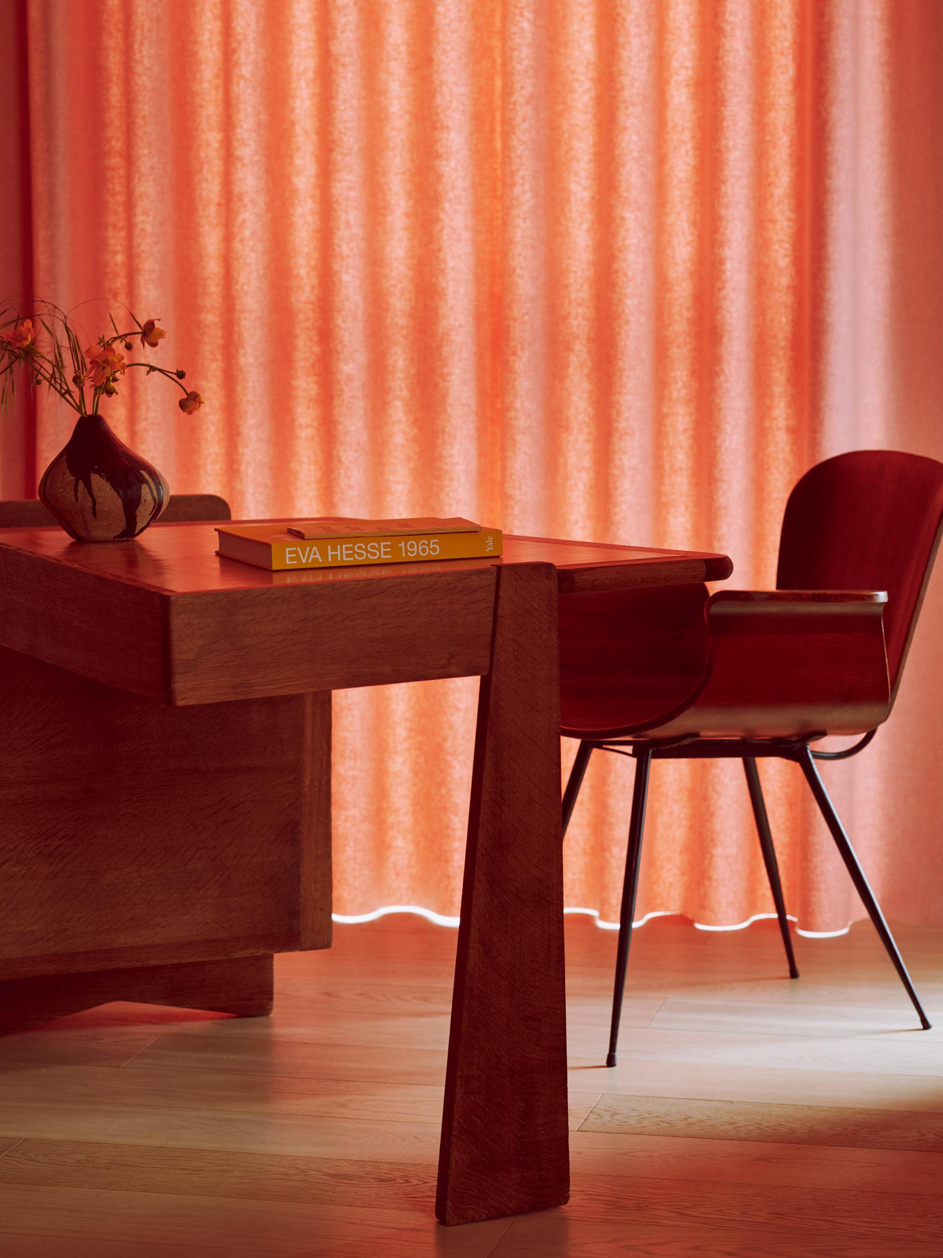 Elegant wooden desk set against warm, textured curtains, featuring a vase and an art book, reflecting Roksanda's curated interiors.