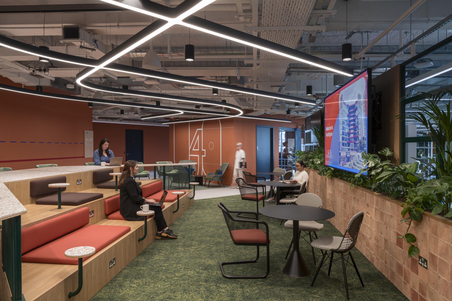 Open workspace of Virgin Media O2's headquarters, featuring modern seating, plants, and a digital display, promoting collaboration and inclusivity.