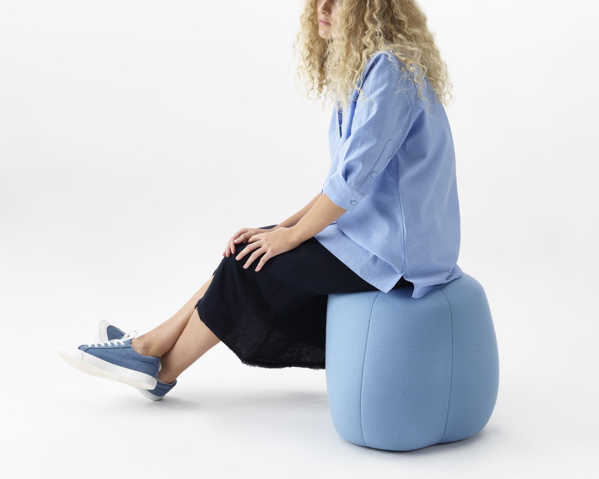 Curvy blue Truffle pouf by NaughtOne with a person seated casually, highlighting its playful and practical design.