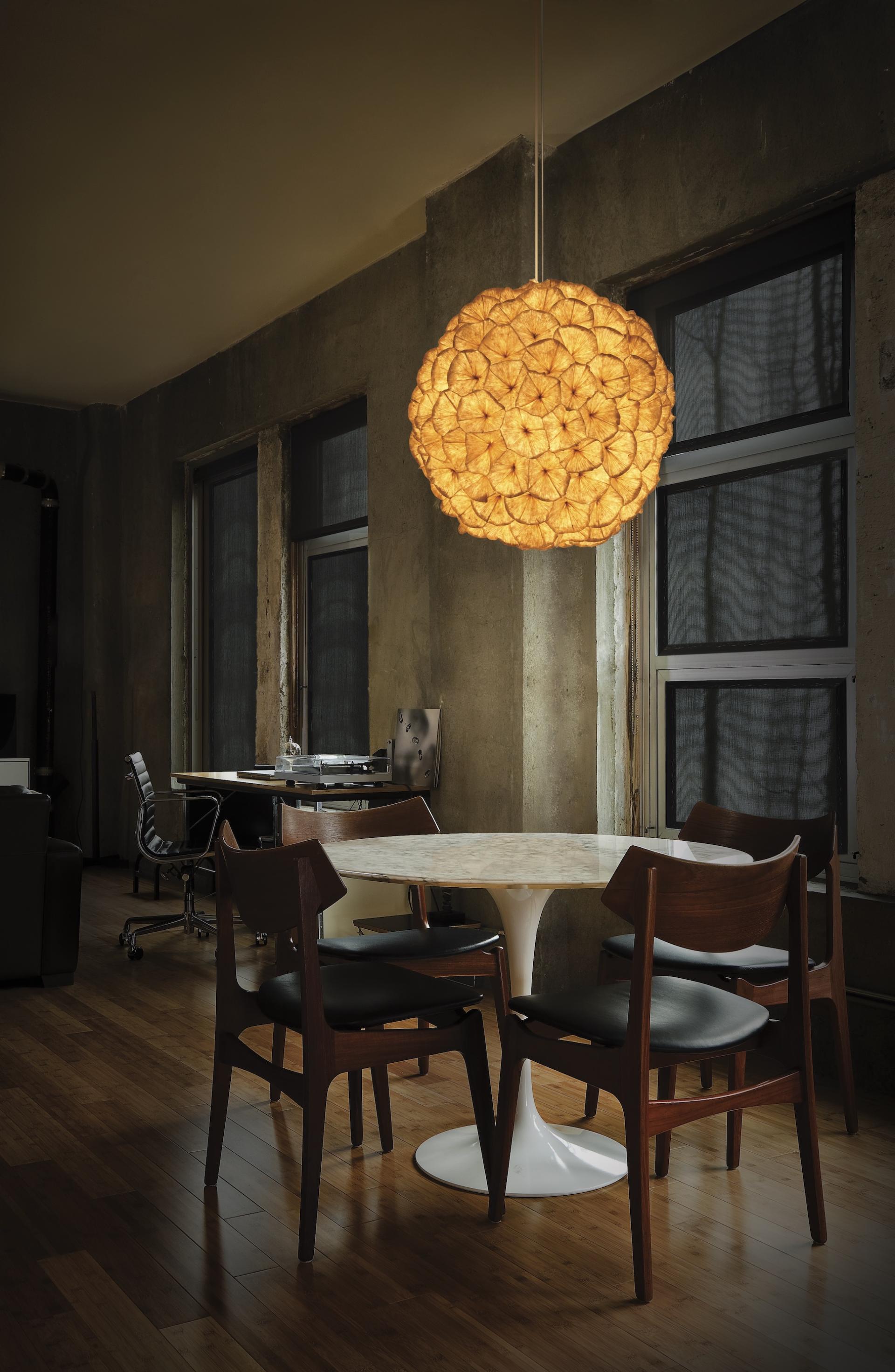 Warm, floral pendant light illuminates a modern dining area with a round table and stylish wooden chairs, evoking spring elegance.
