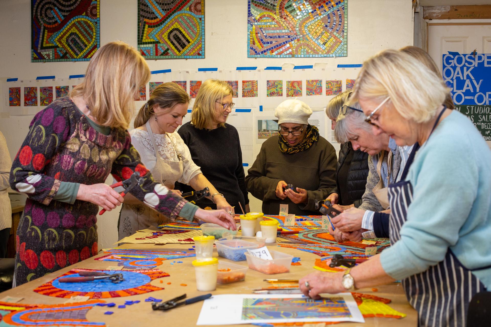 A diverse group of women collaboratively creating a colorful mosaic artwork, celebrating community and traditional craft techniques.