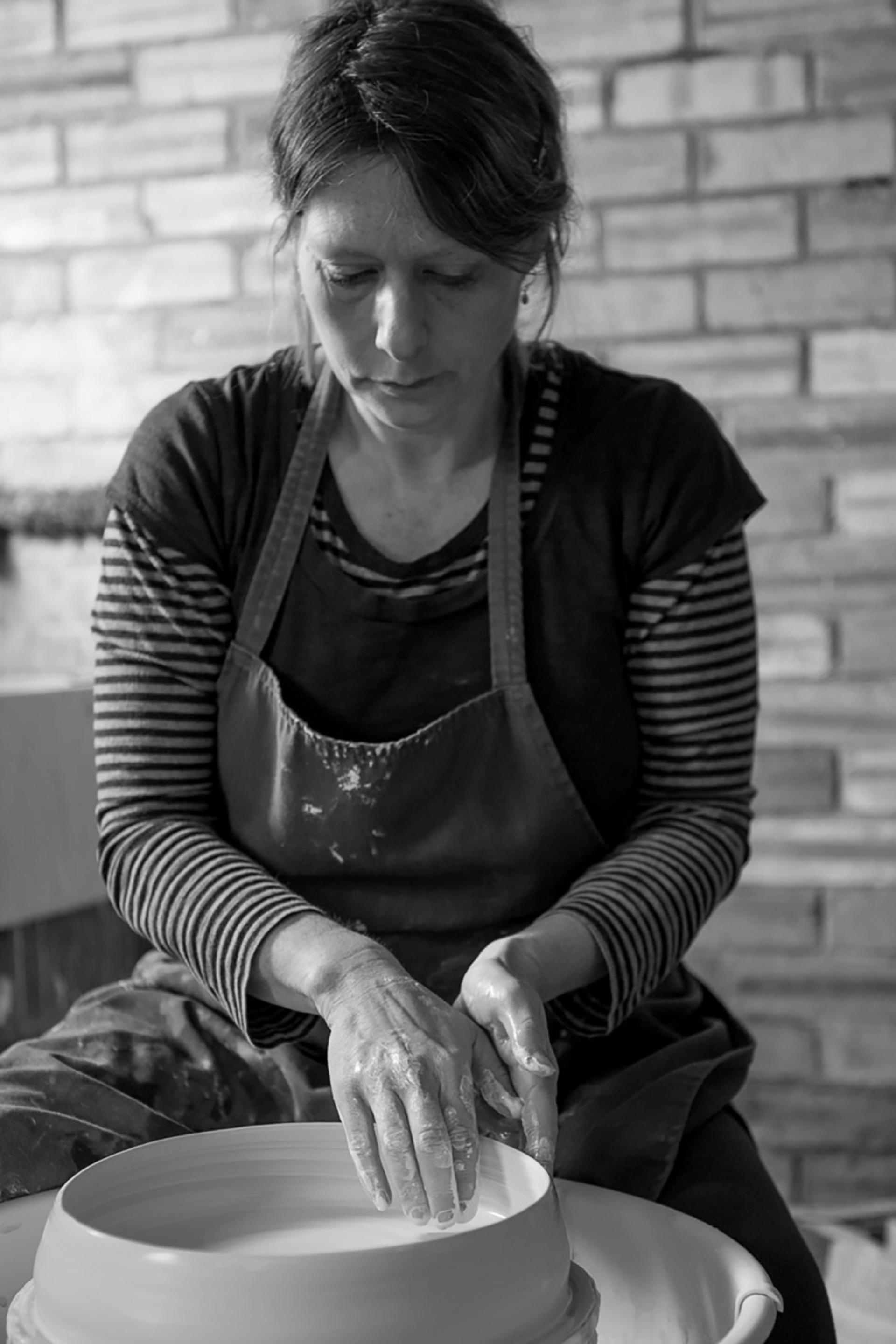 A skilled designer-maker shapes clay on a pottery wheel, showcasing craftsmanship and dedication to the art of design.