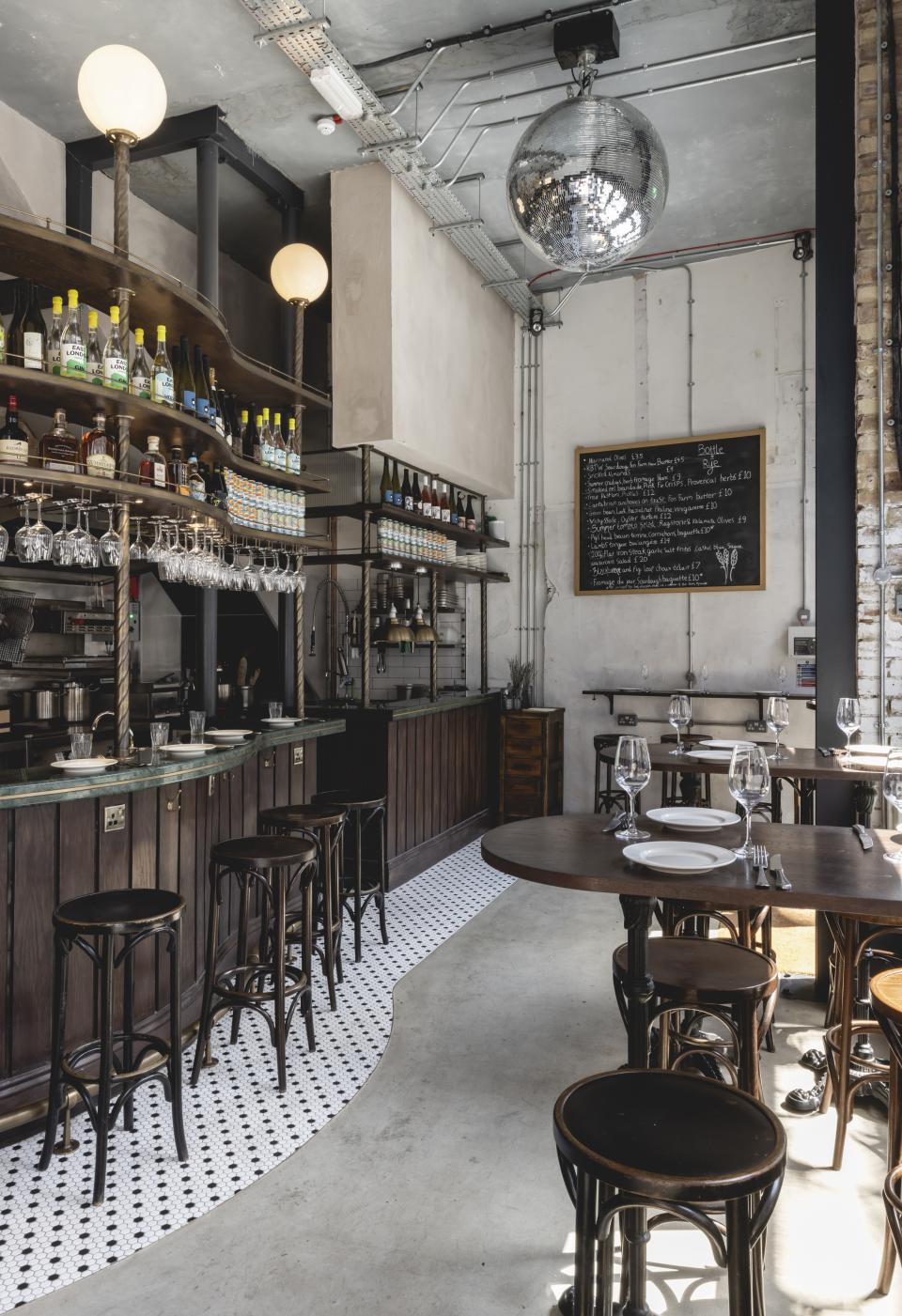 Stylish wine bar and bistro interior featuring a curved bar, high stools, and a disco ball, inspired by Parisian design.