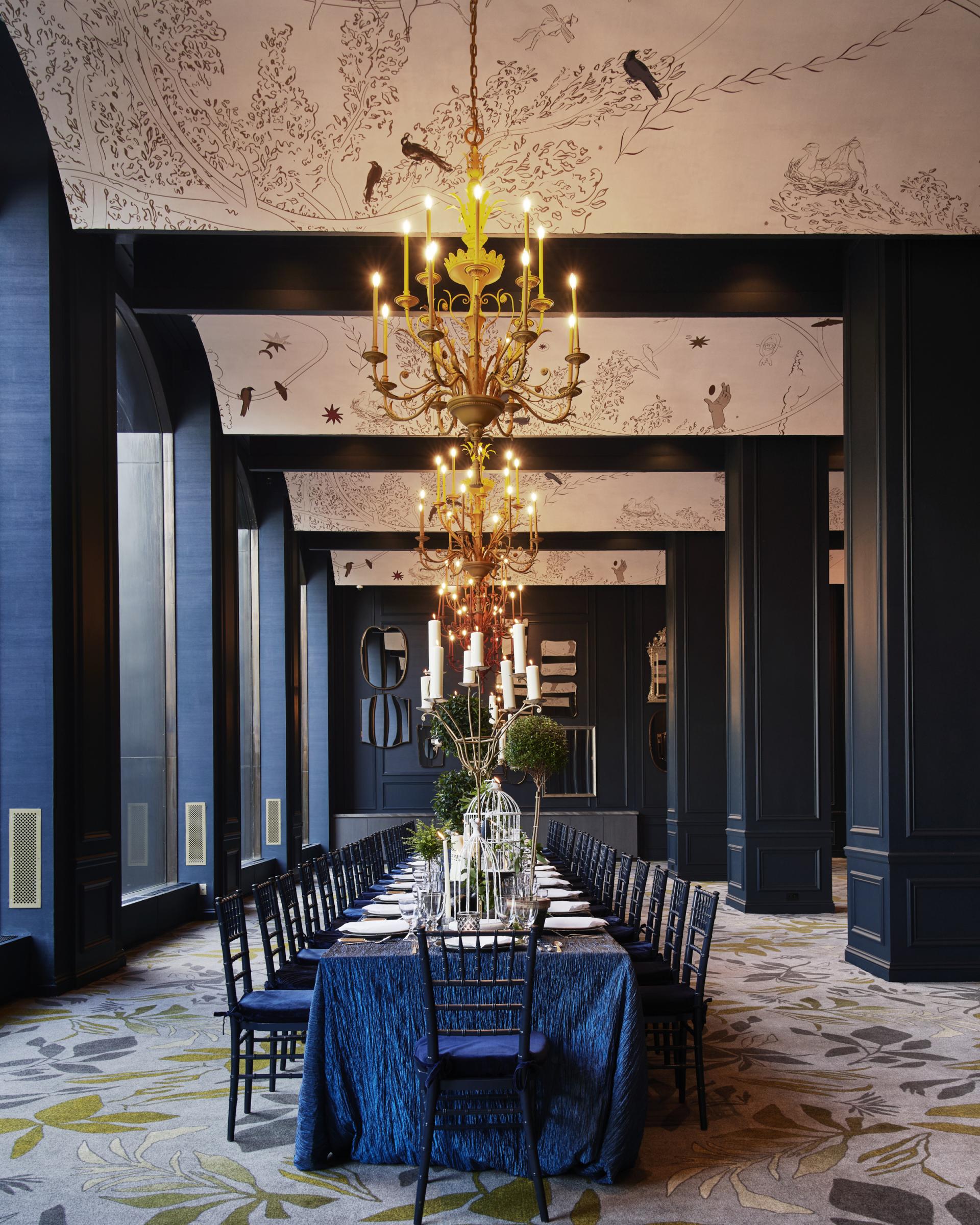 Elegant dining room at Park Lane New York, featuring a chandelier, botanical wallpaper, and a long table set for dining.