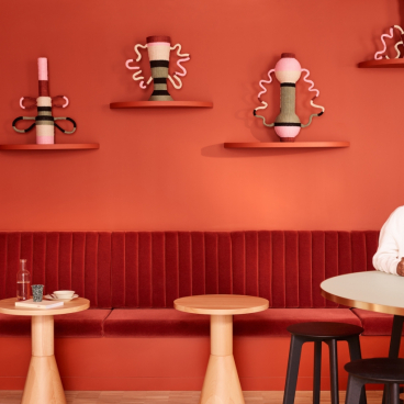 Modern workplace interior featuring cozy seating, vibrant orange walls, and a woman working on a laptop in a creative environment.