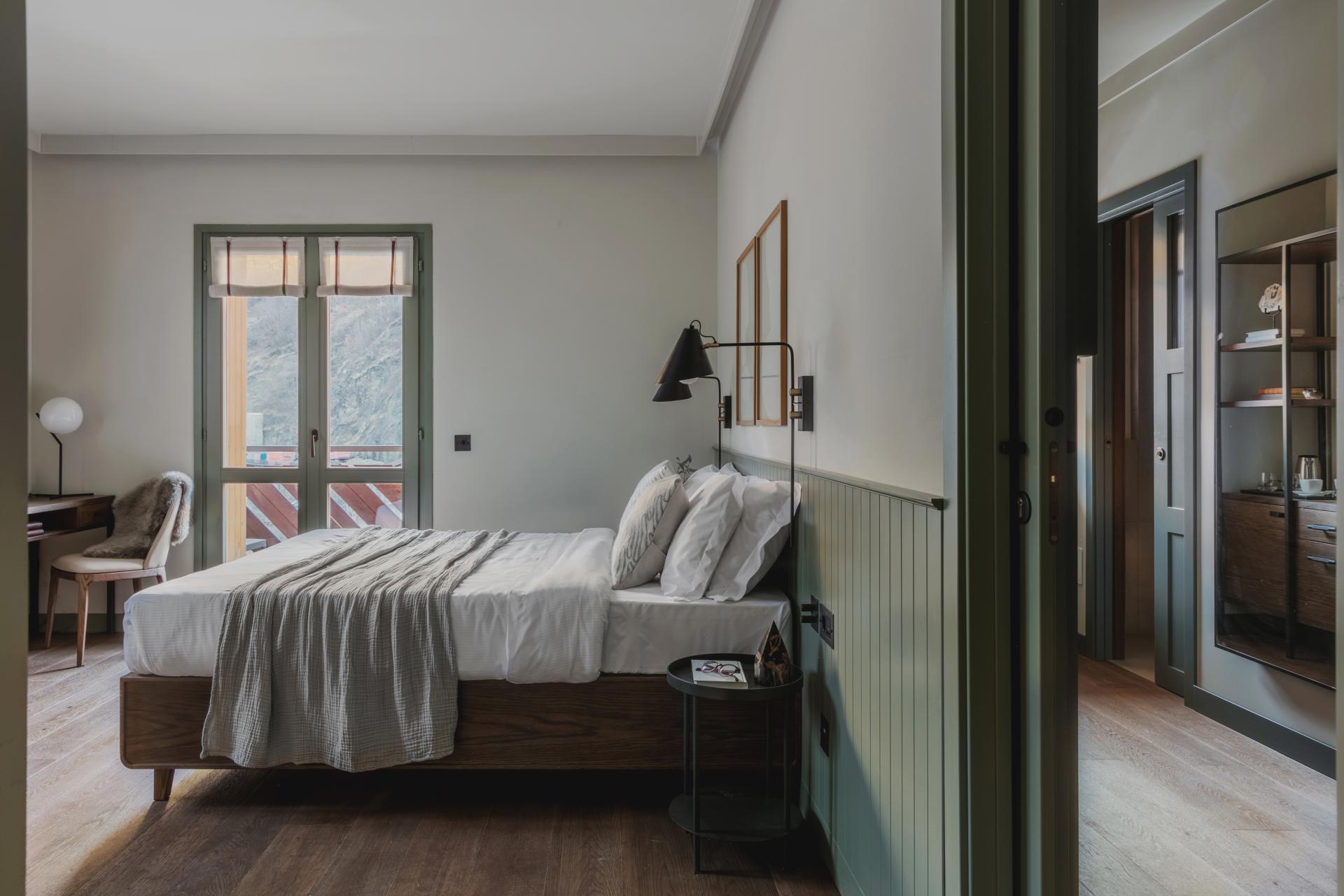 Elegant hotel room featuring a wooden bed, cozy textiles, and natural light from large windows in the Italian mountains.