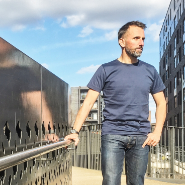David Holt stands thoughtfully on an urban walkway, reflecting Manchester's architectural regeneration and modern design.