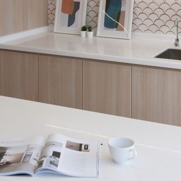Modern kitchen interior featuring minimalist decor, geometric artwork, and a magazine on a white countertop with a coffee cup.