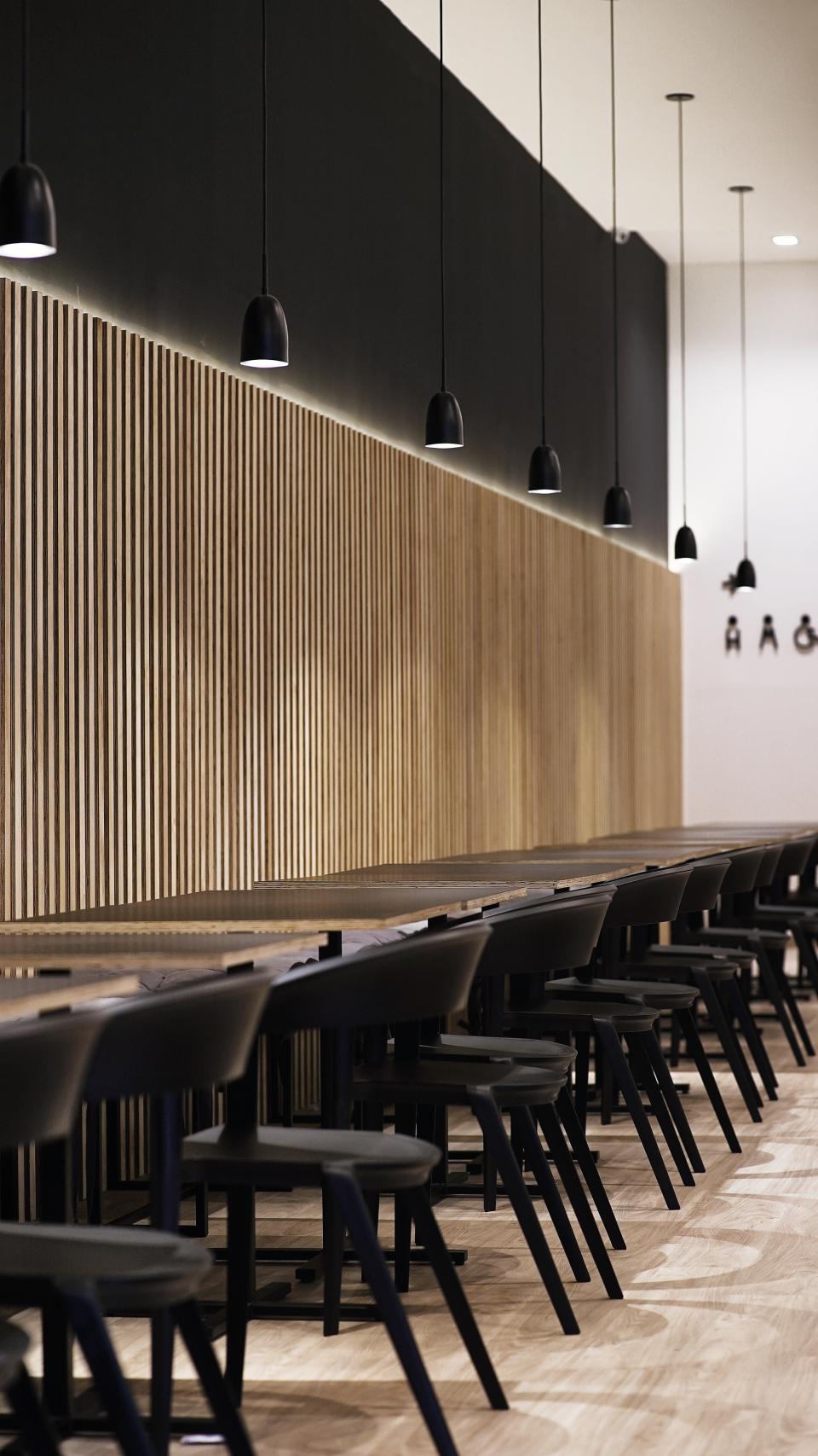 Modern interior of Maru Asian Cuisine featuring wooden paneling, sleek black pendant lights, and minimalist dining tables.