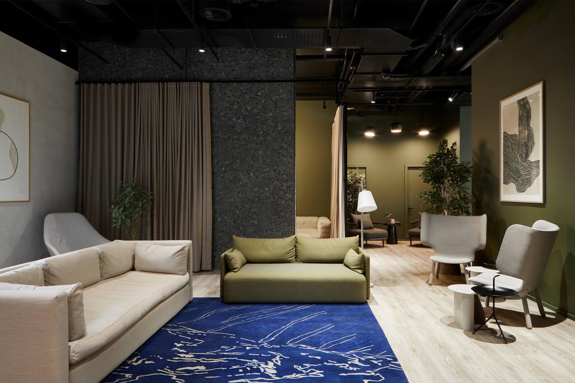 Modern interior design featuring green and beige sofas, decorative plants, and artistic elements in a spacious studio setting.