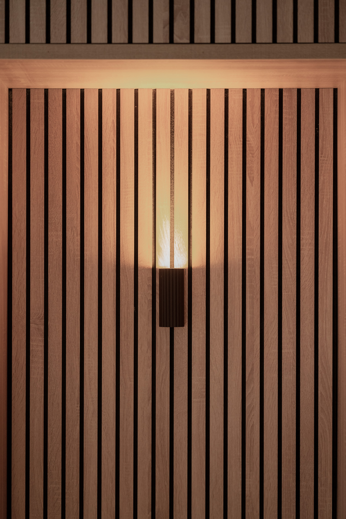 Sophisticated wooden wall paneling with vertical slats and a modern wall light, enhancing interior design at The Place, Nottingham.