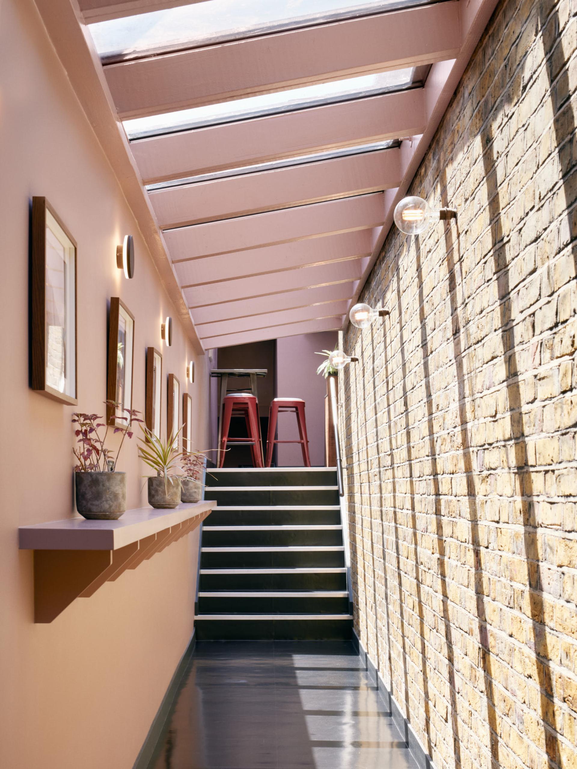 An elegantly designed corridor with a glazed ceiling, featuring brick walls, plants, and modern lighting in The Lexi cinema.