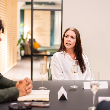 A professional meeting in a modern workspace with diverse participants engaging in discussion and enjoying refreshments.