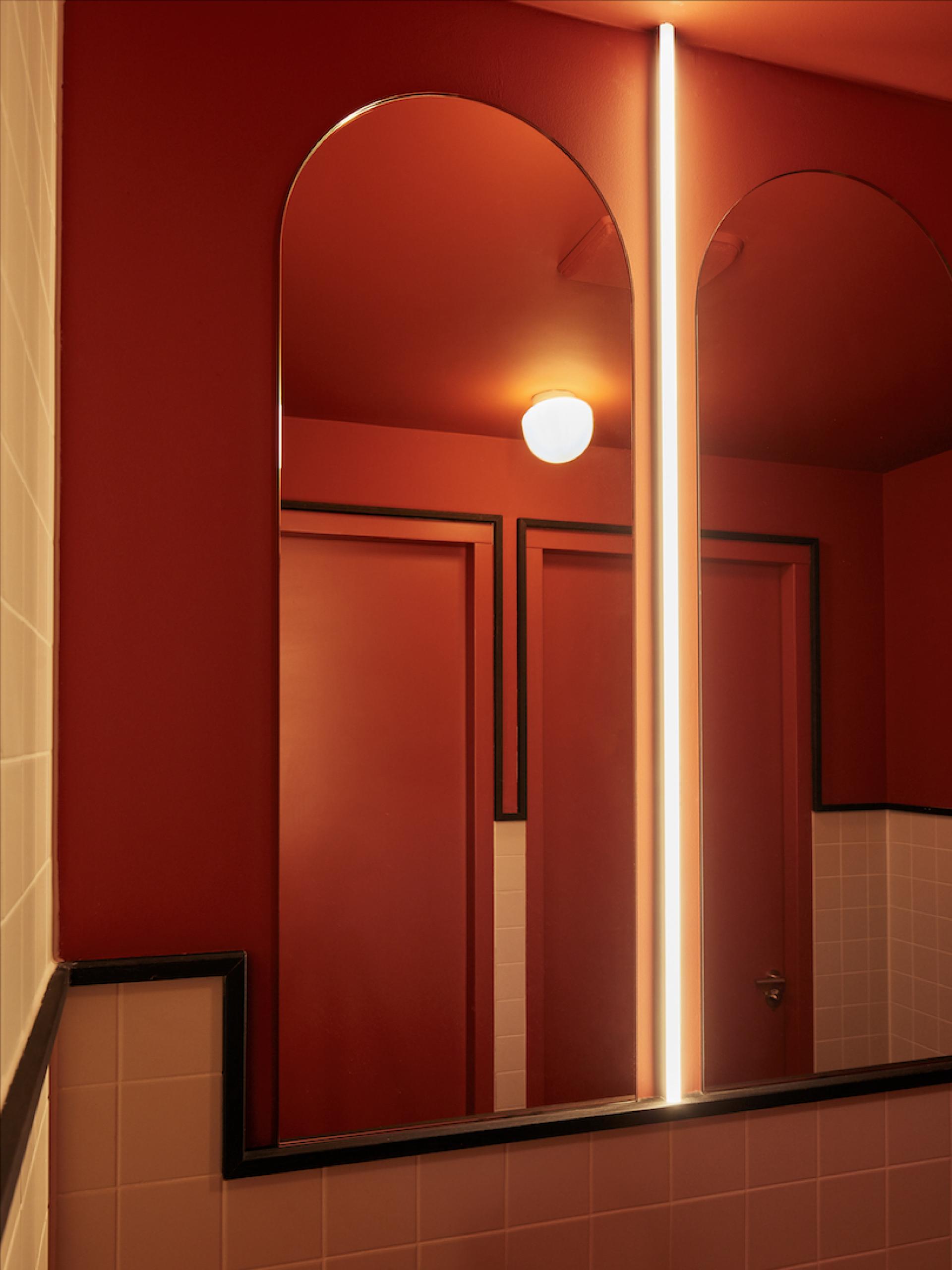 Stylish restroom interior featuring red walls, arched mirrors, and contemporary lighting at Karavaan restaurant in Amsterdam.